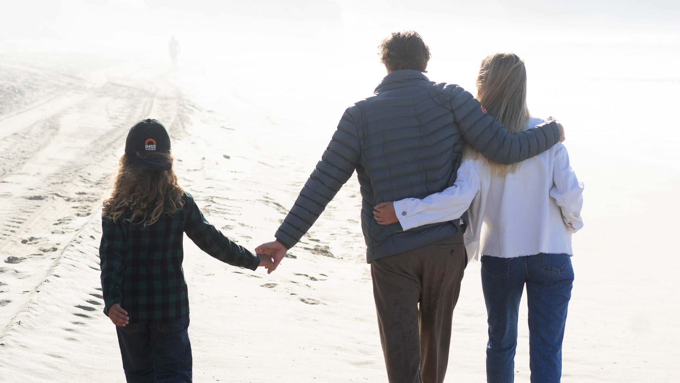 Family walking on a sandy beach, holding hands and enjoying a foggy day by the ocean.