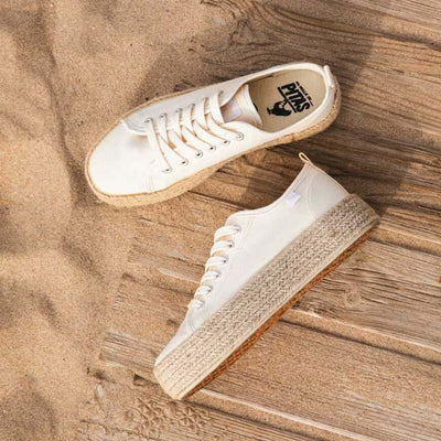 White lace-up 4cm platform espadrille sneakers with jute band on beach setting, showcasing Mediterranean summer style.