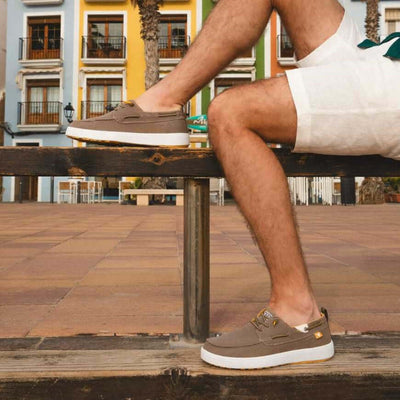 Man wearing Maui Hi-Grip Boat Shoes with elastic laces and hi-grip outsole sitting on a bench in a colorful urban setting.