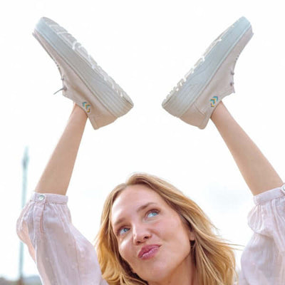 Woman holding Natal Ultralight Platform Wallys in the air, showcasing breathable cotton upper and ultralight EVA platform sole.